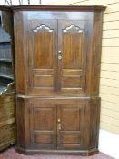 AN ANTIQUE OAK TWO PIECE STANDING CORNER CUPBOARD, twin upper and lower doors having shaped and