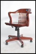 A 20th century stained beech captains office chair raised on a wheeled five point base with