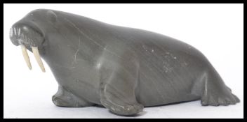 An Inuit / Eskimo soapstone carving of a walrus with two walrus ivory tusks. Signed to base B.I. ( B