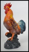 A vintage style cast iron figurine of a cockerel raised on a naturalistic base being painted.