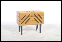 A vintage mid 20th century retro metamorphic sewing box being raised on ebonised tapering legs