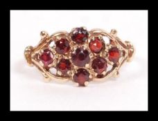 A hallmarked 9ct gold and garnet cluster ring having an antique style scroll setting. Hallmarked