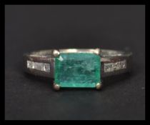 A 14ct white gold emerald and diamond ring having a central faceted emerald with diamond encrusted