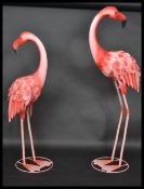 A pair of patterned metal garden ornament flamingos having a painted pink feathered finish.