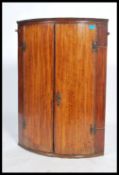 A 19th century Georgian bow fronted oak hanging corner cabinet having a pair of full length doors