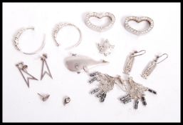 A collection of silver to include a pair of silver atomic earrings, silver whale brooch, silver leaf
