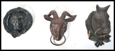 A group of three cast iron door knockers one in the form of a lion one being a ram and one being a