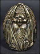 A brass vesta case in the form of a bat hiding within its wings.
