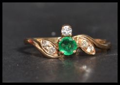 An 18ct gold diamond and emerald crossover ring having a central emerald stone with diamond leaves