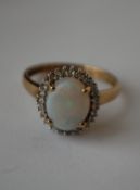 A hallmarked 9ct gold ring set with a central opal surrounded by a diamond halo. Diamonds approx