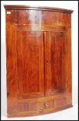 A late Georgian wall hanging bow fronted corner cabinet in mahogany having twin doors to reveal a