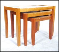 A retro teak wood Danish inspired nest of three tiled top tables, raised on square legs united by