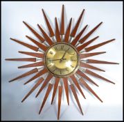 A vintage mid century teak wood sunburst wall clock. The gilded dial with roman numeral chapter ring