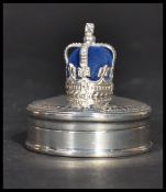 A sterling silver pill box of circular form having a blue baize pin cushion atop in the form of a