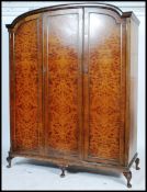 A Queen Anne revival triple wardrobe compactum in burr walnut being raised on cabriole legs with pad