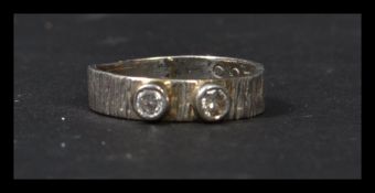A diamond and platinum band ring being set with two bezel set diamonds having bark decoration to the