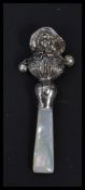 A sterling silver babies rattle in the form of a lady with mother of pearl handle.