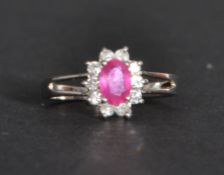 An 18 ct white gold ruby and diamond ring having a central ruby with a halo of white stones. Size