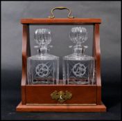 A mahogany and brass mounted twin bottle Tantalus having fold out front with swing handle atop.