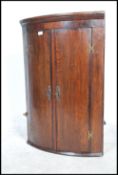 A Georgian 19th century hanging bow fronted oak corner cabinet having flared cornice over twin