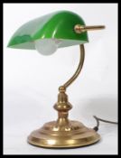 A vintage 20th century bankers desk lamp having an adjustable green glass shade raised on a brass