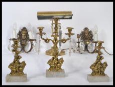 An early 20th century 3 piece garniture of brass and marble candelabra, each adorned with putti to