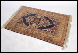 A vintage early 20th century floor rug decorated with plants and fauna to the central blue ground