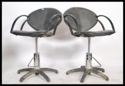 A pair of retro style barbers stools, black leatherette upholstery raised on an adjustable chromed