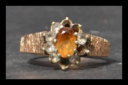 A hallmarked 9ct gold ring having bark effect shoulders with a central orange stone with a halo of