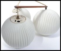 A vintage retro 20th century boomerang ceiling light having three milk glass shades on a teak