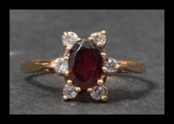 A hallmarked 9ct gold ring set with an oval mixed cut garnet surrounded by a halo of white stones.