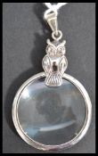 A sterling silver magnifying glass pendant having an owl bail loop atop.