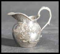 A silver hallmarked creamer being chase decorated and cast in relief with scrolls having a shaped