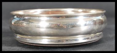 A silver hallmarked wine bottle stand having inset ring turned wooden base. The raised gallery