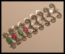 A sterling silver marcasite bracelet of scrolled form set with rubies and emeralds. Weighs 30