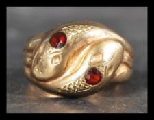 A hallmarked 9ct gold ring in the form of entwined coiled snakes having orange stone eyes.