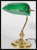 A vintage 20th century bankers desk lamp having an adjustable green glass shade raised on a brass