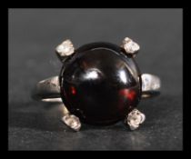 A hallmarked 9ct white gold ring set with a garnet cabochon with four white accent stones.