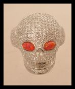 A sterling silver dress ring in the form of a skull having inset red stone eyes with many CZ