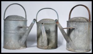 A collection of three vintage 20th Century galvanised metal watering cans, some with impressed