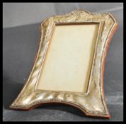 An early 20th century hallmarked silver easel back picture frame of serpentine shape being decorated
