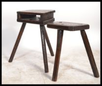 Two early 20th century oak ebonised milking stools on tripod legs with panel seats. One having