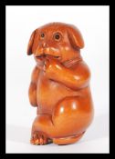 A Japanese carved wooden netsuke in the form of a dog with hand to mouth.