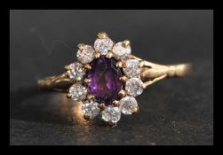 A hallmarked 9ct gold cluster ring having a central purple oval cut stone surrounded by white
