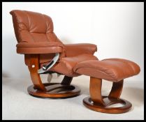 A Stressless style brown leather reclining armchair and matching ottoman raised on a faux wood