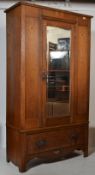An  Edwardian Arts & Crafts light oak wardrobe  having a plinth drawer base with central mirror door