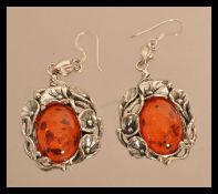 A pair of sterling silver and amber earrings having central amber cabochons with floral silver