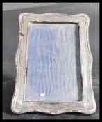 An early 20th century hallmarked silver easel back picture frame of serpentine shape being