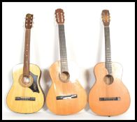 A group of three vintage acoustic six string guitars having shaped hollow bodies with paper labels