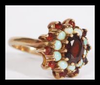 A hallmarked 9ct gold opal and garnet stone cluster ring having a central faceted red stone with a